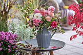 Strauß aus Rosen (Rosa), Schneebeeren (Symphoricarpos)  und Wildem Wein in Vase auf der Terrasse