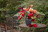 Herbstlicher Strauß aus Dahlien (Dahlia), Myrtenaster, Rosen, orientalischer Knöterich, Gartenfuchsschwanz (Amaranthus caudatus) auf Gartentisch