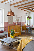 Open-plan living room with cot, macramé wall hanging and wooden beamed ceiling