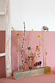 Dried flower arrangement in rustic wooden block in front of pink wall