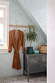 Chest of drawers with houseplant, straw basket and bathrobe on coat rail