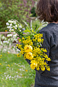 Woman holding bouquet of flowers with bird cherry, rapeseed, summer snowflake 'Gravetye Giant', tulip 'Strong Gold' and woolly yarrow