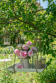 Bouquet of peonies (Paeonia) in vase hanging on tray in tree