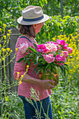 Frau mit Strauß aus Pfingstrosen (Paeonia) im Garten