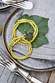 Napkin rings made of branches on a green leaf and patterned cloth napkin with ivy berries next to silver cutlery