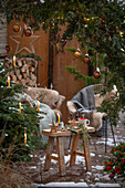 Weihnachtlich rustikal geschmückte Terrasse mit Sitzplatz vor Thuje und Christbaum mit Anhängern
