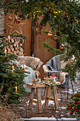 Weihnachtlich rustikal geschmückte Terrasse mit Sitzplatz vor Thuje und Christbaum mit Anhängern