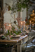 Weihnachtlich festlich gedeckter Tisch im Hüttenstil, Kiefernzapfen, Tannenzweige, Kerzenständer, Hirschfiguren, Christbaum