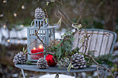 Laterne auf Gartentisch mit Kieferzapfen, Christbaumkugeln, Haselzweigen