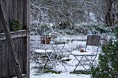 Hemlock wreath on barn door in front of snowy garden with seating area