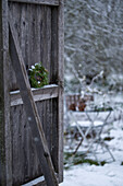 Hemlock wreath on barn door in front of snow-covered garden with seating area