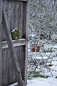Hemlock wreath on barn door in front of snow-covered garden with seating area