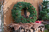 Kranz aus Kiefer und Zapfen mit Fell und Hirschgeweih auf Holzstapel