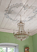 Crystal chandelier with ornate decorations on the wooden ceiling in green-painted room