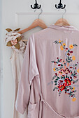 Kimono with floral embroidery and silk dress on wooden hangers on hooks