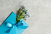 Blue envelope with forget-me-nots (Myosotis) on a light grey background