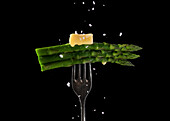 Green asparagus spears, topped with melting butter an sprinkled with salt .on a fork