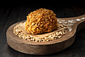 A single scotch egg on a wooden spoon and a bed of pearl barley.