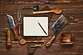 Notebook surrounded by barbecue cutlery on a wooden table