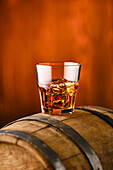 Whisky on the rocks in a tumbler on a wooden barrel