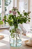 Flowers in glass vase on light-coloured wooden table in front of window