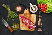 Raw lamb steak on chopping board with spices and kitchen utensils