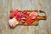 Various types of sausage and ham on a wooden board