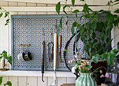 Wall with hooks and garden utensils, next to it a flower vase and plants