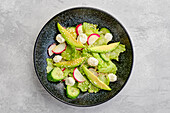 Top view of salad with lettuce, avocado, radish and mozzarella dressed with sesame