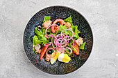 Top view of salad with lettuce, salmon, tomato, boiled egg and onion with olives