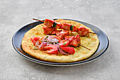 Shashlik skewers on flatbread with tomatoes and red onions