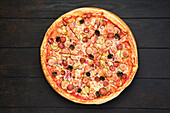 Pizza with various kind of thin sausages, pickled cucumber, olives and red onion, top view