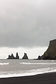 Black sand beach with Reynisdrangar basalt sea stacks and cliffs in background on cloudy day, near Vik i Myrdal, Iceland
