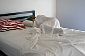 Schlafende Frau unter weißem Leinenbettzeug bei Tageslicht mit rot-weiß gestreiften Kissen auf der linken Seite