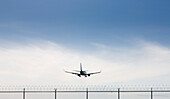 Rear view of Commercial Airplane flying over barbed wire fence