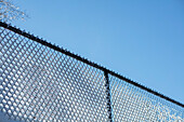Low angle view of snow on chain link fence against blue sky