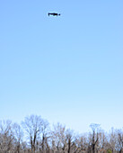 Kleine Drohne schwebt in der Luft vor einem blauen Himmel mit kahlen Bäumen am Horizont