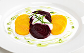 Sliced yellow and purple beets with chives and crème fraiche, drizzled with olive oil on white plate