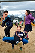Grönland, Nordwestküste, Qaanaaq oder New Thule, Inuit-Kinder spielen in ihrer Pause auf einem Spielplatz, im Hintergrund ein Eisberg
