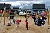 Grönland, Nordwestküste, Baffinsee, Qaanaaq oder New Thule, Inuit-Kinder spielen in der Pause auf einem Spielplatz, im Hintergrund ein Eisberg