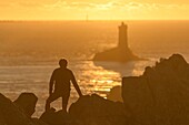 Frankreich, Finistere, Plogoff, Wanderer bei Sonnenuntergang an der Pointe du Raz, im Hintergrund der Leuchtturm der Vieille
