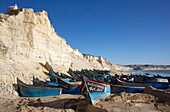 Marokko, Westsahara, Dakhla, blaue Fischerboote, die am Strand von Araiche gestrandet sind, gesäumt von einer Klippe