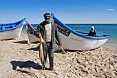 Marokko, Westsahara, Dakhla, Fischer mit einem Oktopus in der Hand vor einem Boot am Strand