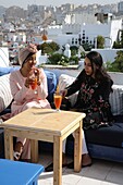 Marokko, Tanger Region Tetouan, Tanger, zwei junge Marokkanerinnen im Retro-Look trinken Fruchtsaft auf der Terrasse des Cafe le Salon bleu mit Blick auf die Kasbah