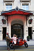 Frankreich, Paris, Royal Monceau Hotel, Frau fährt in einem Retro-Seitenwagen vor der Hotelfassade, bewacht von zwei Dienern