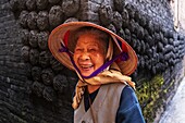 Vietnam, Hanoi province, Bat Trang, the village of ceramists, smiling woman in front of lumps of charcoal stuck on a wall of a traditional house