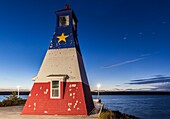 Canada, Nova Scotia, Cabot Trail, Cheticamp, town harbor with lighthouse painted in traditional Acadian colors, dusk