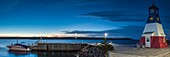 Canada, Nova Scotia, Cabot Trail, Cheticamp, town harbor with lighthouse painted in traditional Acadian colors, dusk