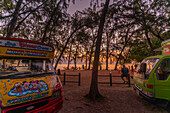 Blick auf Menschen am öffentlichen Strand von Mon Choisy bei Sonnenuntergang, Mauritius, Indischer Ozean, Afrika