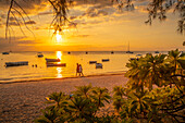 Blick auf Boote und Menschen am öffentlichen Strand von Mon Choisy bei Sonnenuntergang, Mauritius, Indischer Ozean, Afrika
